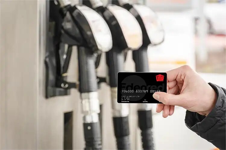 Hand mit UTA Edenred Tankkarte vor Zapfsäulen